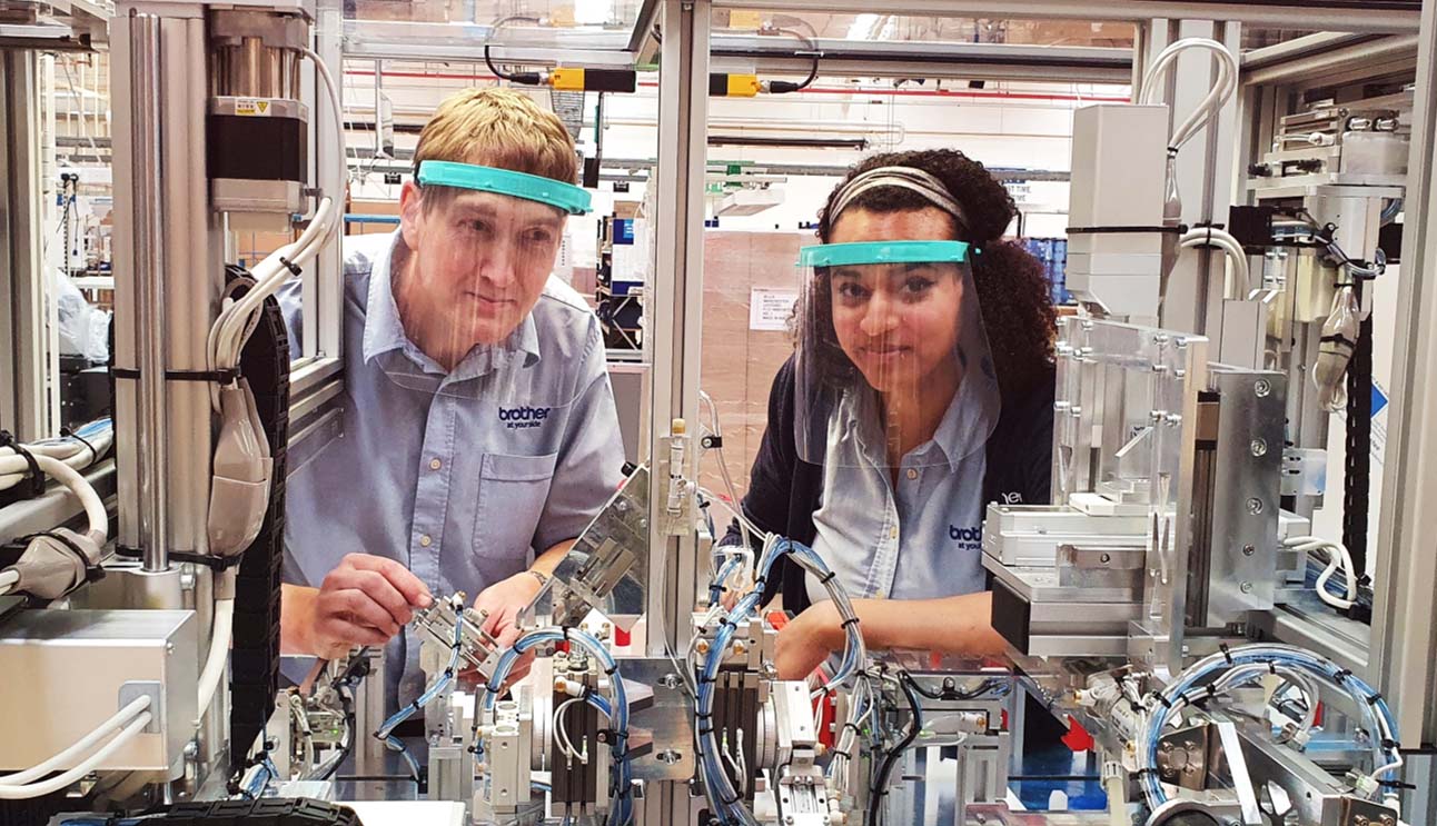 Two Brother Industries UK Robotic engineers working on one of their projects, due to being in close contact they are wearing Brother Industries manufactres face visors to ensure safety due to the recent COVID-19 crisis around the world