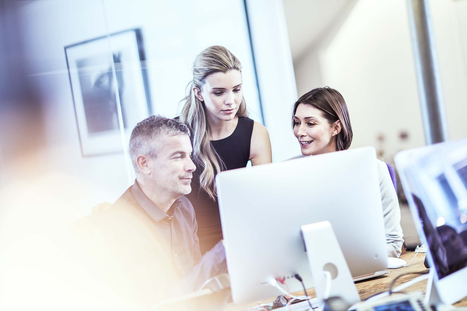 Image of a group of staff gathered around a large computer monitor discussing a project